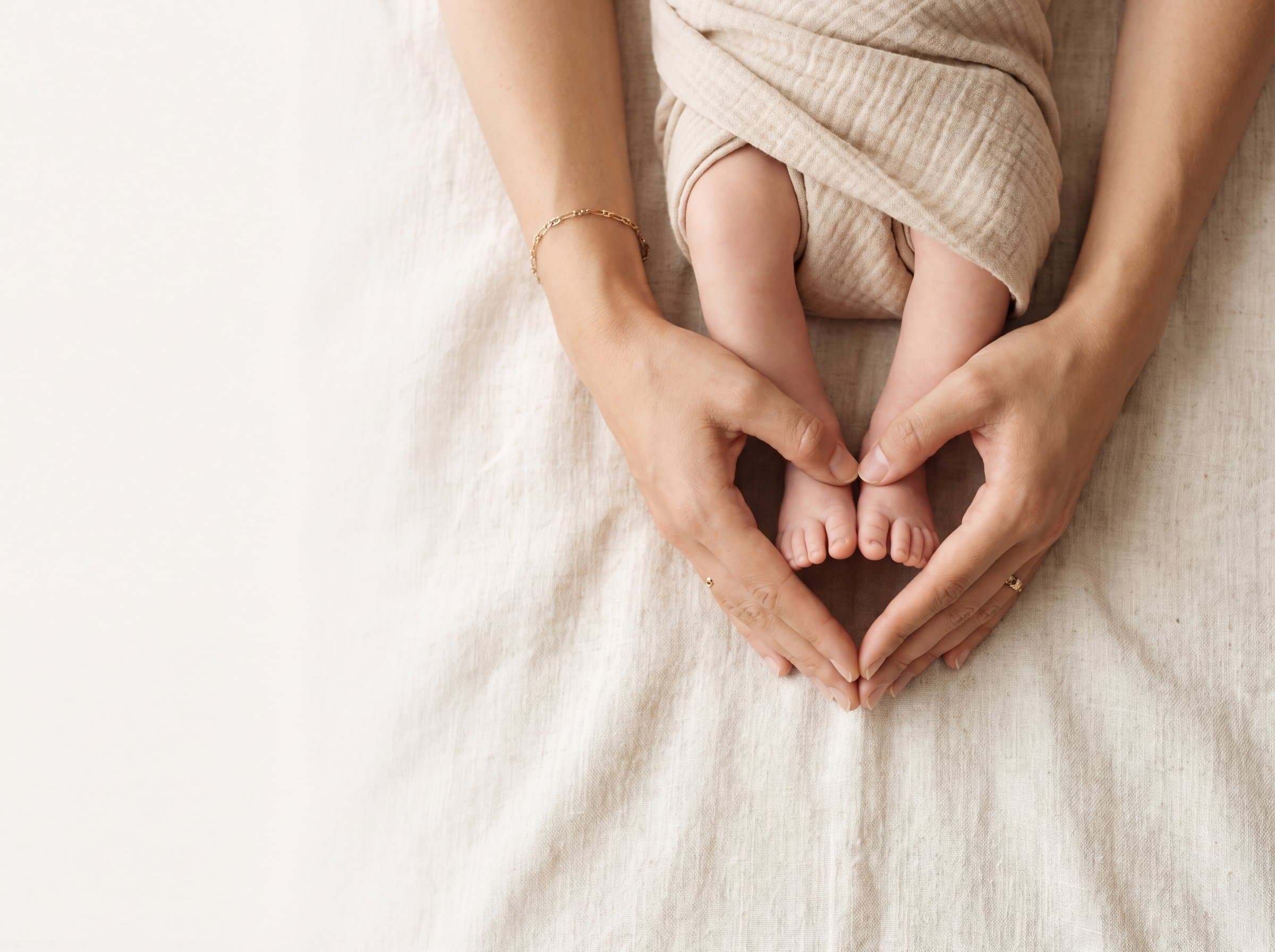 Mother's hands cradling baby's feet on soft linen