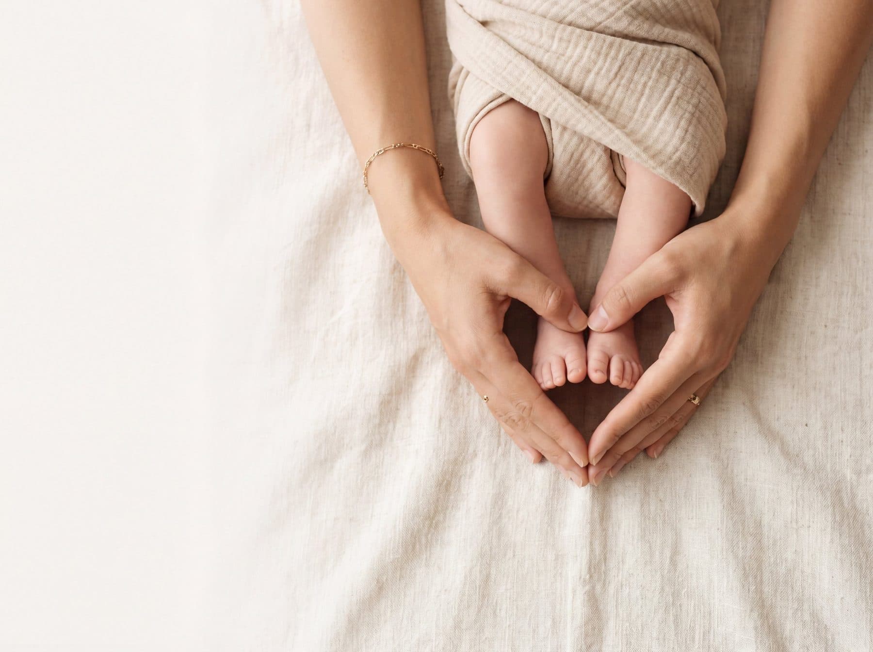Mother's hands cradling baby's feet on soft linen